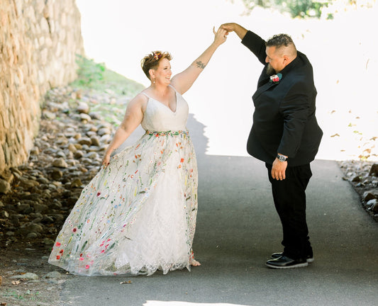 Beautiful happy couple on their wedding day dancing. Bride is wearing a 130cm long colourful floral overskirt over her white wedding dress.